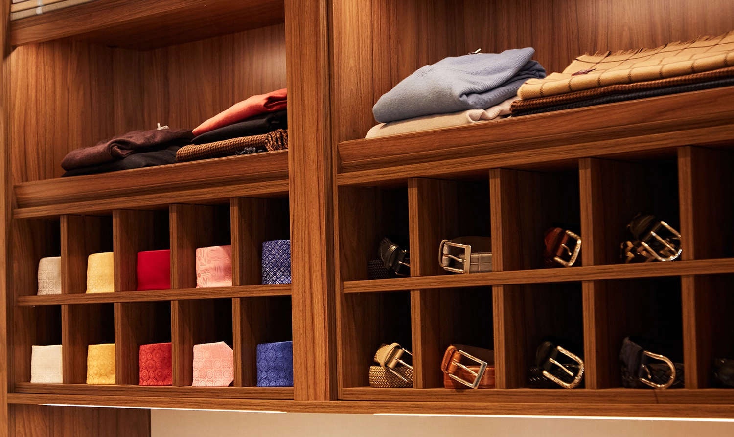 Cashmere knits, folded silks, and belts arranged in walnut cubbies