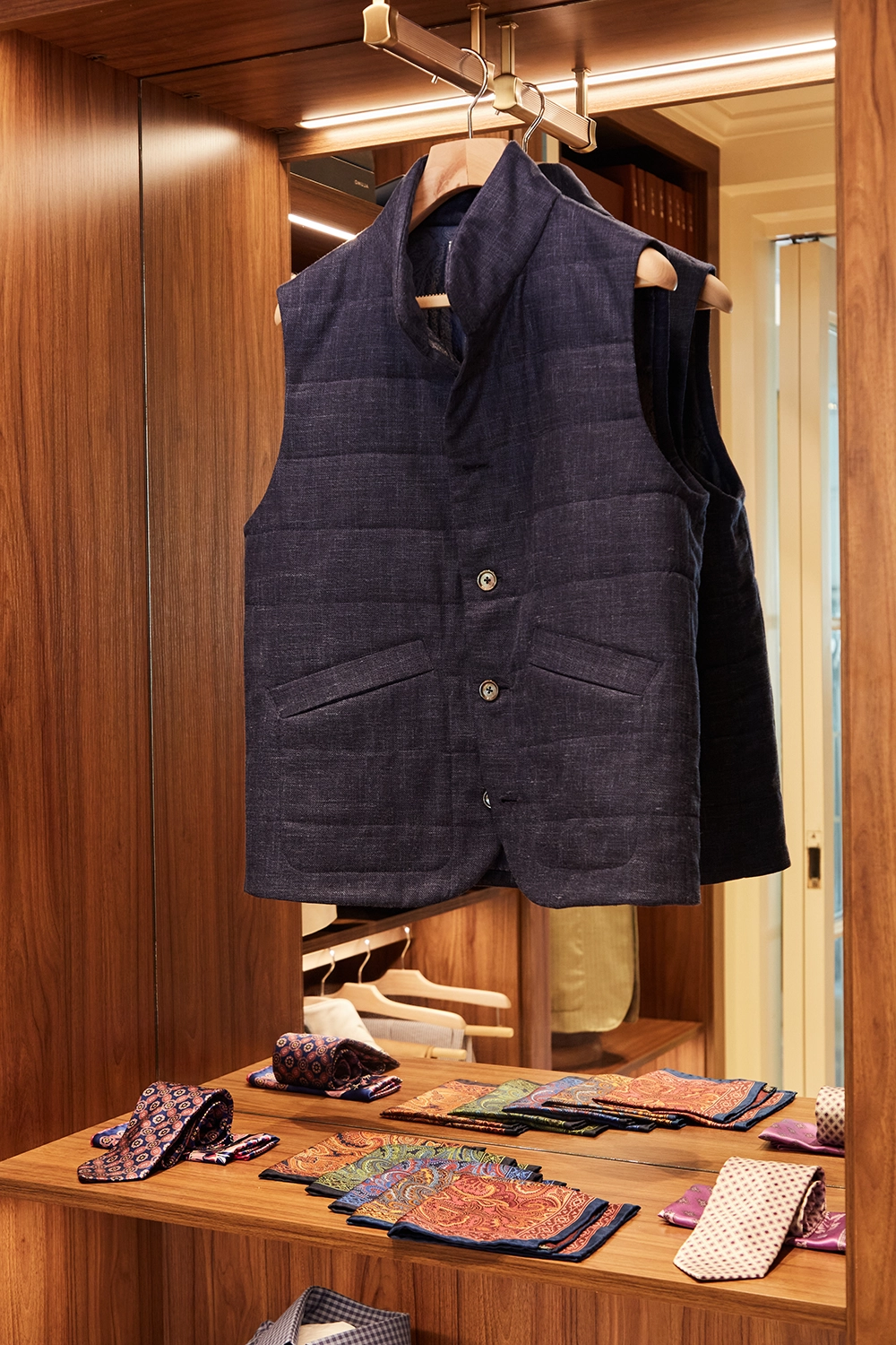 A linen-blend gilet on a brass rail above folded silks